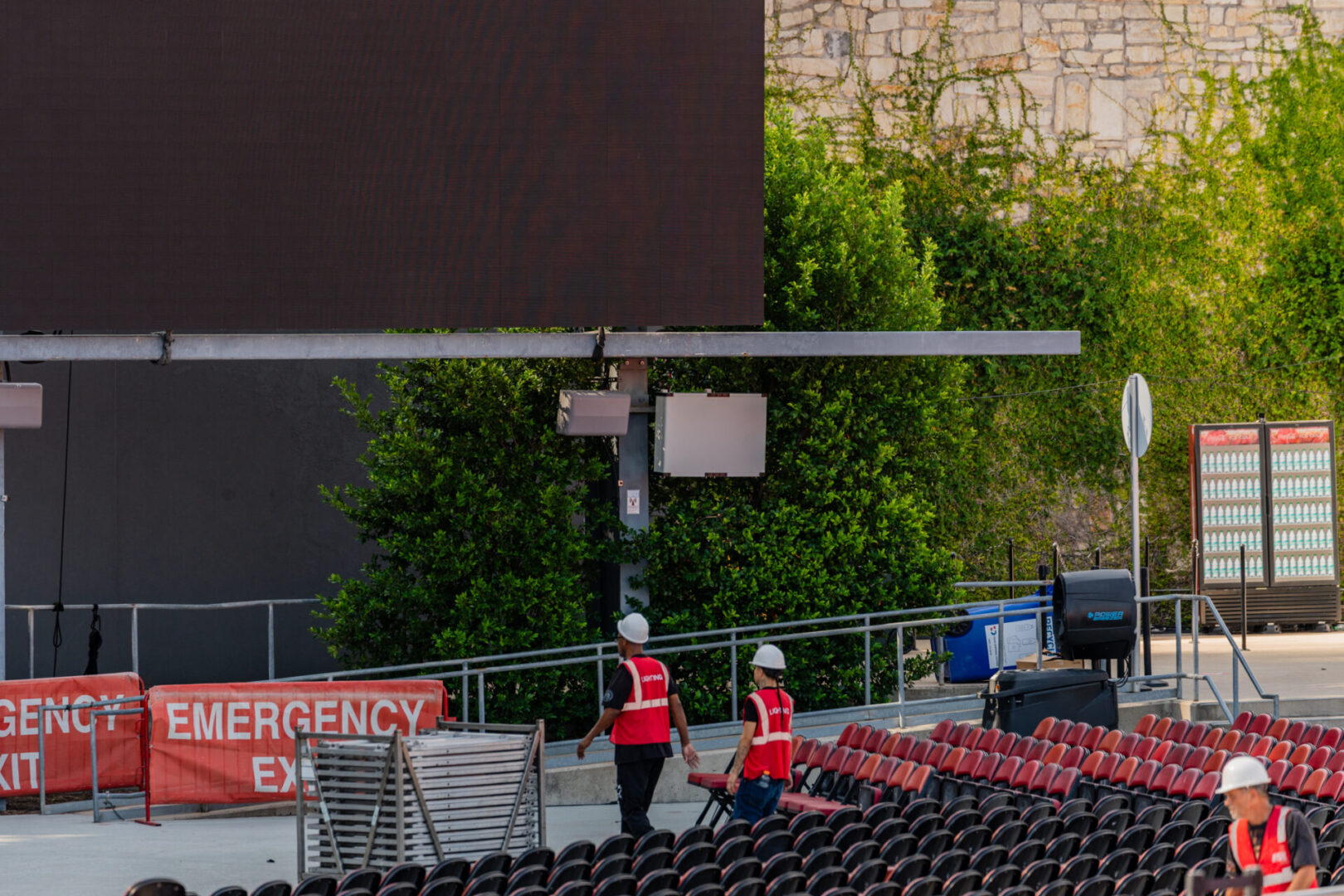 Workers setting up equipment near a building and greenery.