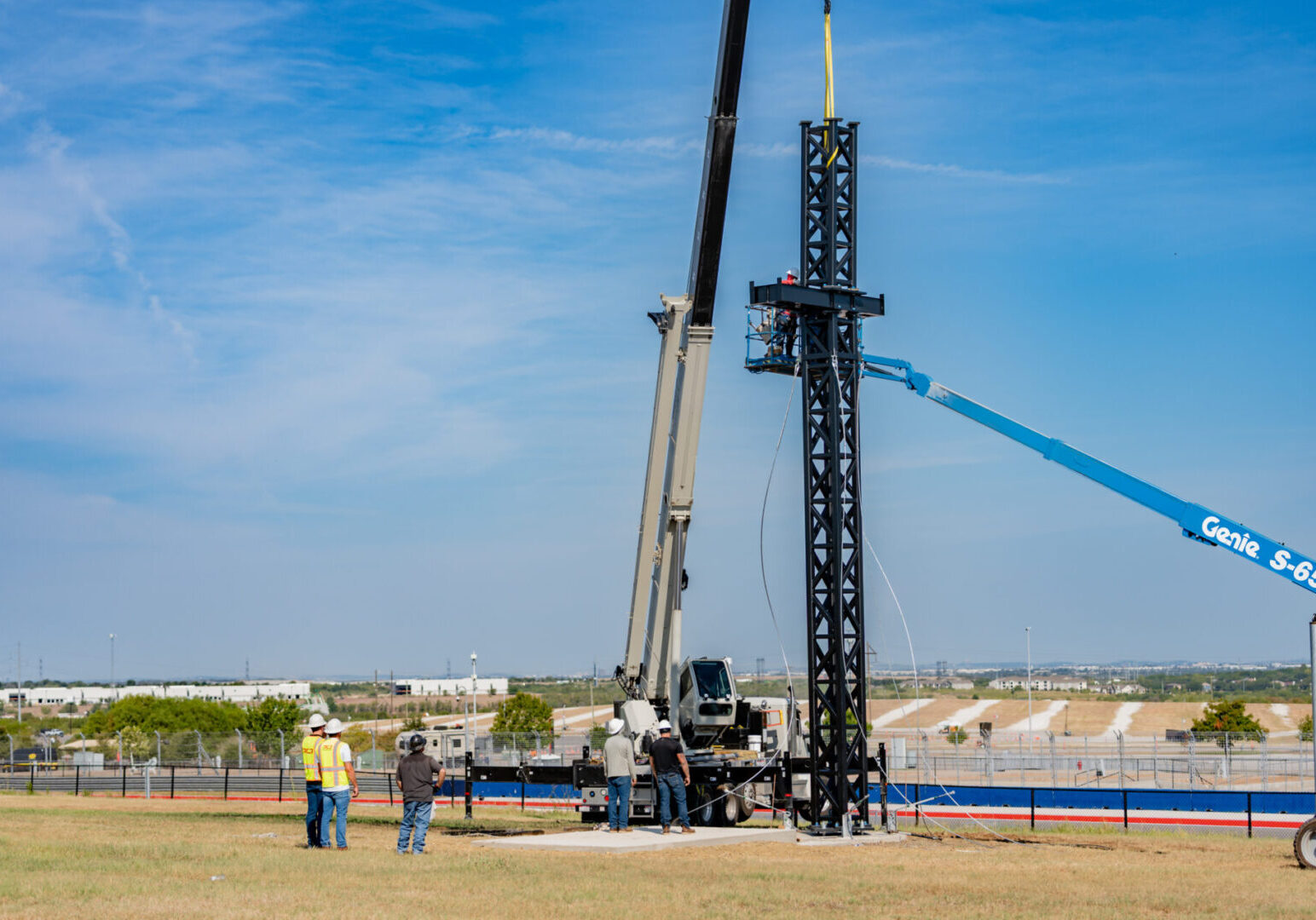 Construction workers using cranes to erect a tall metal structure outdoors.