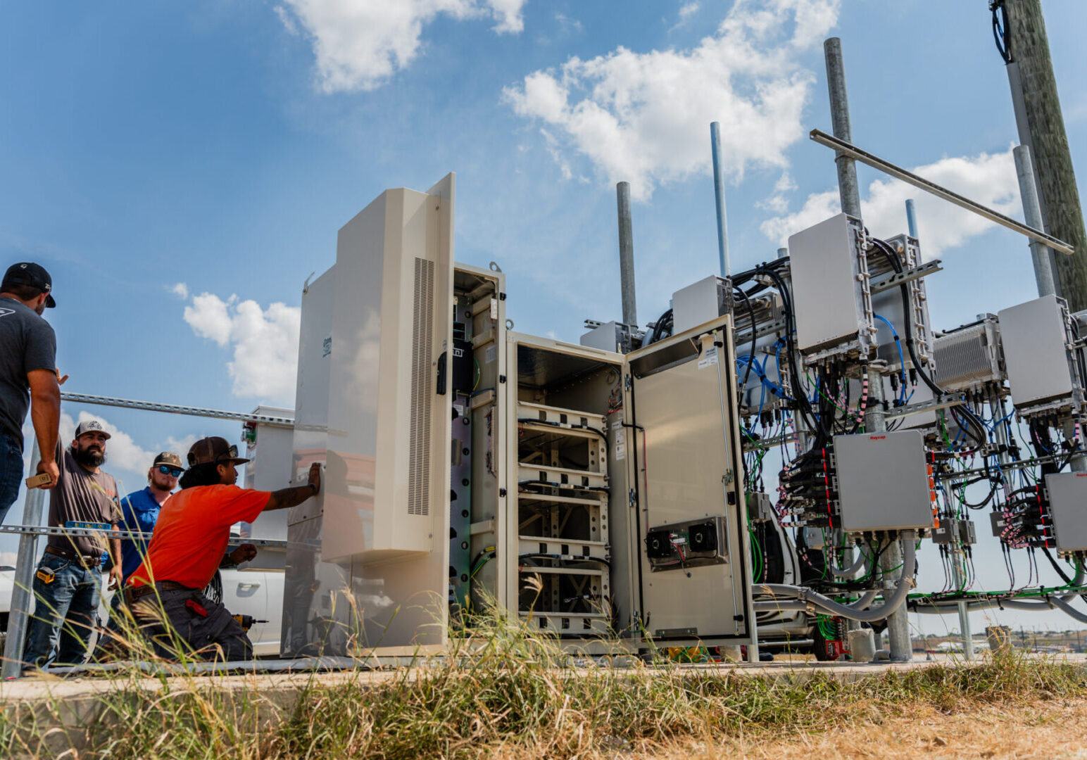 Technician working on outdoor telecom equipment under a blue sky.